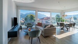 A modern living room with a flat-screen TV, a sofa, chairs, a dining table, and large windows offering mountain views. - Modern House Apartment 4, Menaggio, Italy (Menaggio)