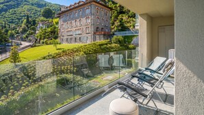 A balcony with a glass railing overlooking a mountainous landscape, a stone building, and a clear sky. - Modern House Apartment 4, Menaggio, Italy (Menaggio)
