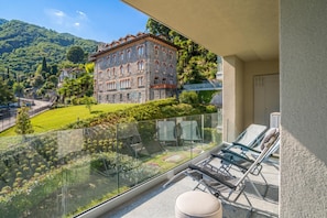 A balcony with a glass railing overlooking a mountainous landscape, a stone building, and a clear sky. - Modern House Apartment 4, Menaggio, Italy (Menaggio)