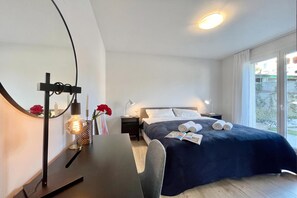 A hotel room with a bed, bedside tables, a desk, a mirror, and a window.