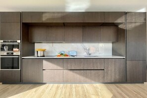 A modern kitchen with built-in appliances, a marble backsplash, and wooden cabinetry.