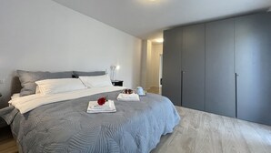 Une chambre à coucher moderne avec un grand lit, une literie grise, une table de chevet avec une lampe et une armoire.