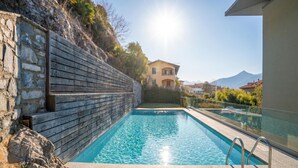 Une piscine bordée d’un mur en pierre, offrant une vue dégagée sur une montagne en arrière-plan.