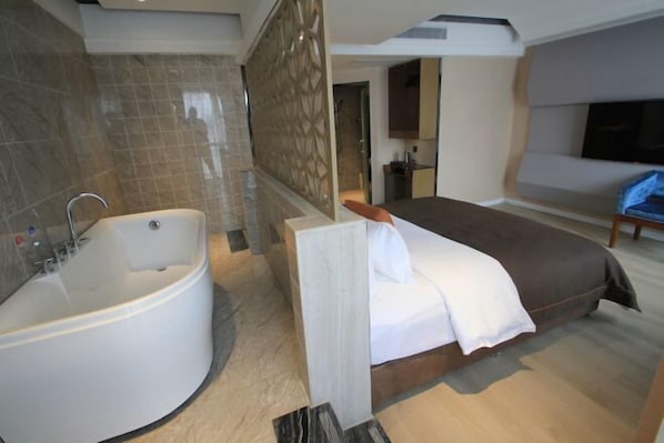 Habitació d'hotel moderna amb un llit gran, un bany separat amb banyera i un televisió de pantalla plana penjada a la pared.