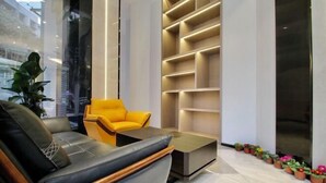 A modern lobby with a leather sofa, a yellow armchair, and a built-in shelving unit. - sinweier hotel (Mianyang)