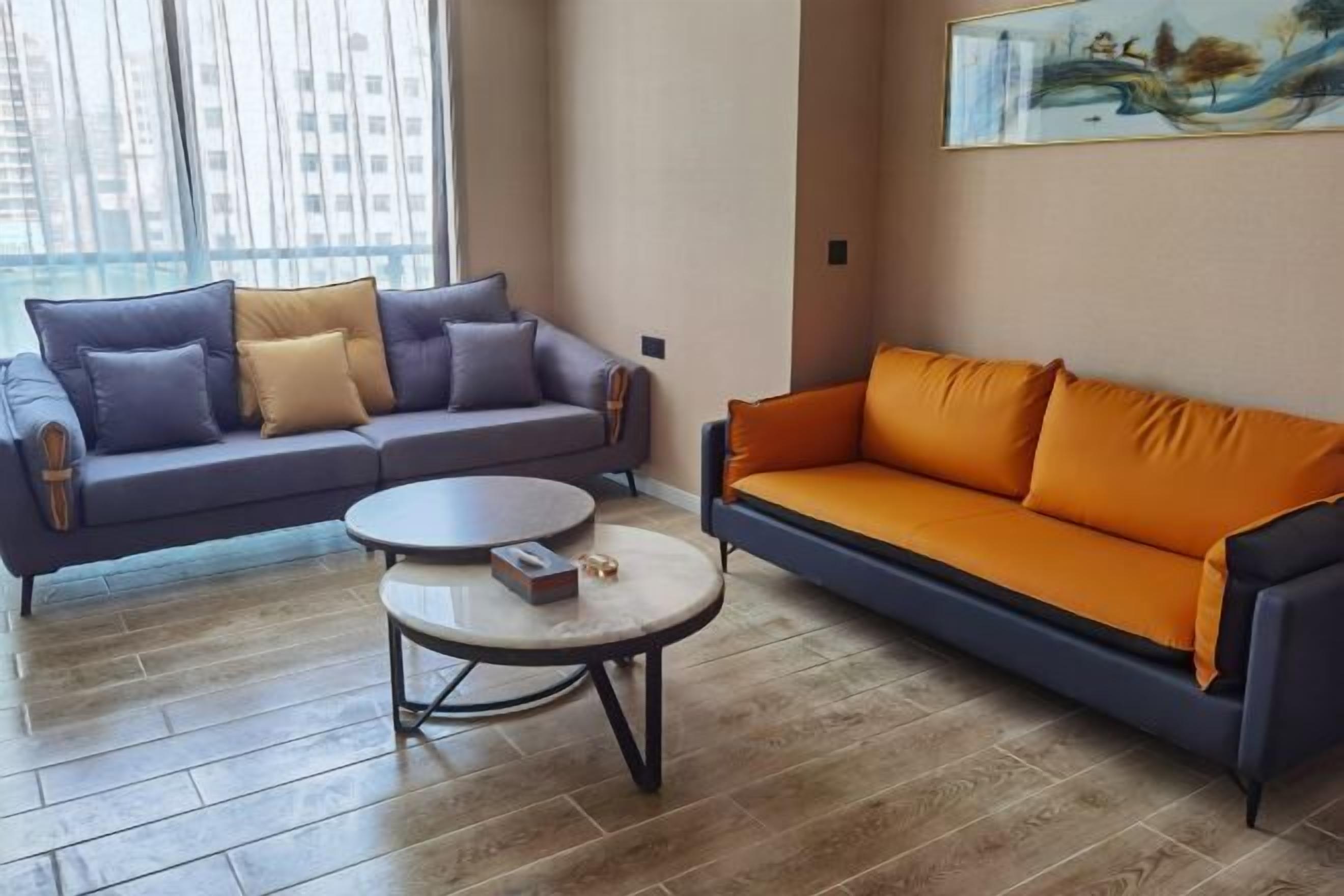 A living room with two sofas, one grey and one orange, a round coffee table, and a painting on the wall.