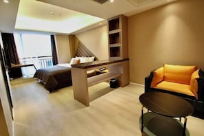 Habitació d'hotel moderna amb un llit, un sofà, una taula petita i un balcó amb barana.