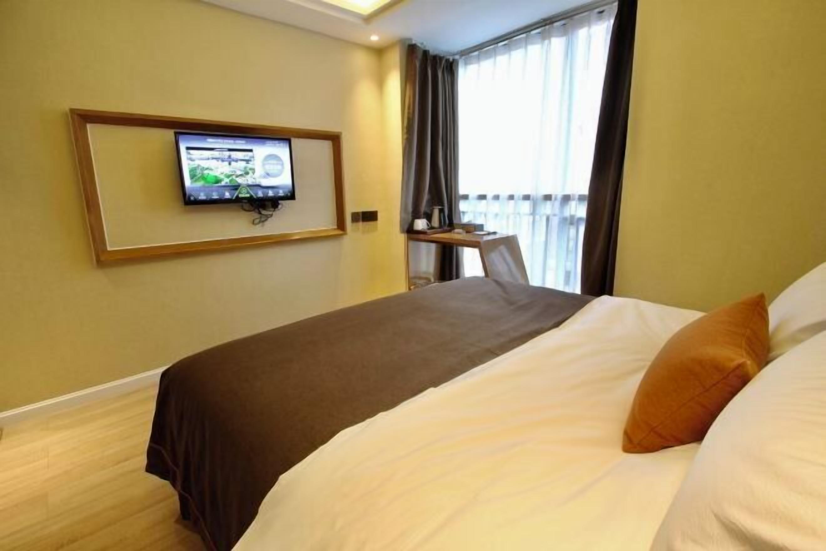 Habitación de hotel con cama, televisor en la pared, una mesita y una ventana con cortinas.