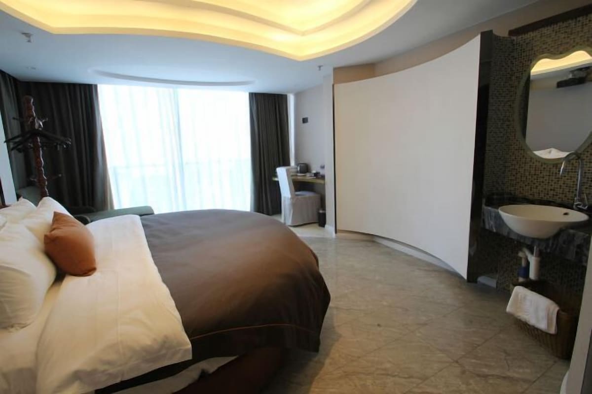 Habitació d'hotel amb un llit gran, un escriptori, un bany amb un lavabo i una finestra gran.