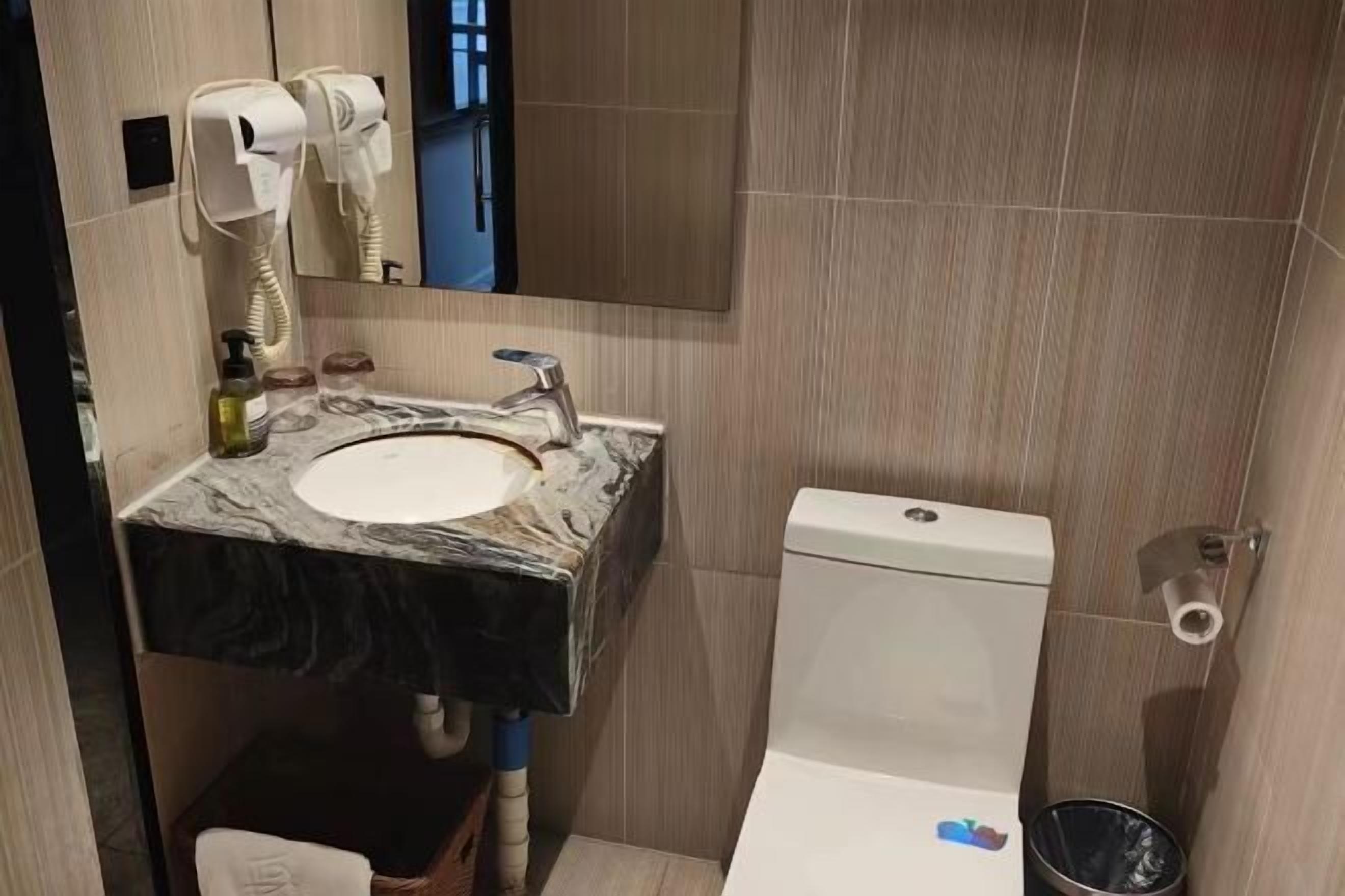 A bathroom with a marble sink, a toilet, and a hairdryer on the wall.