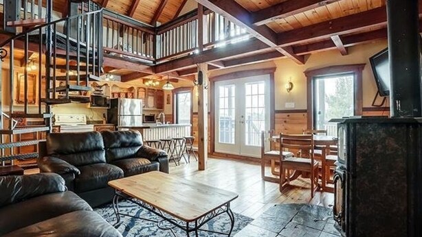 Un vaste espace de vie doté d’un haut plafond, d’un escalier, d’une cheminée et d’une cuisine située au fond de la pièce.