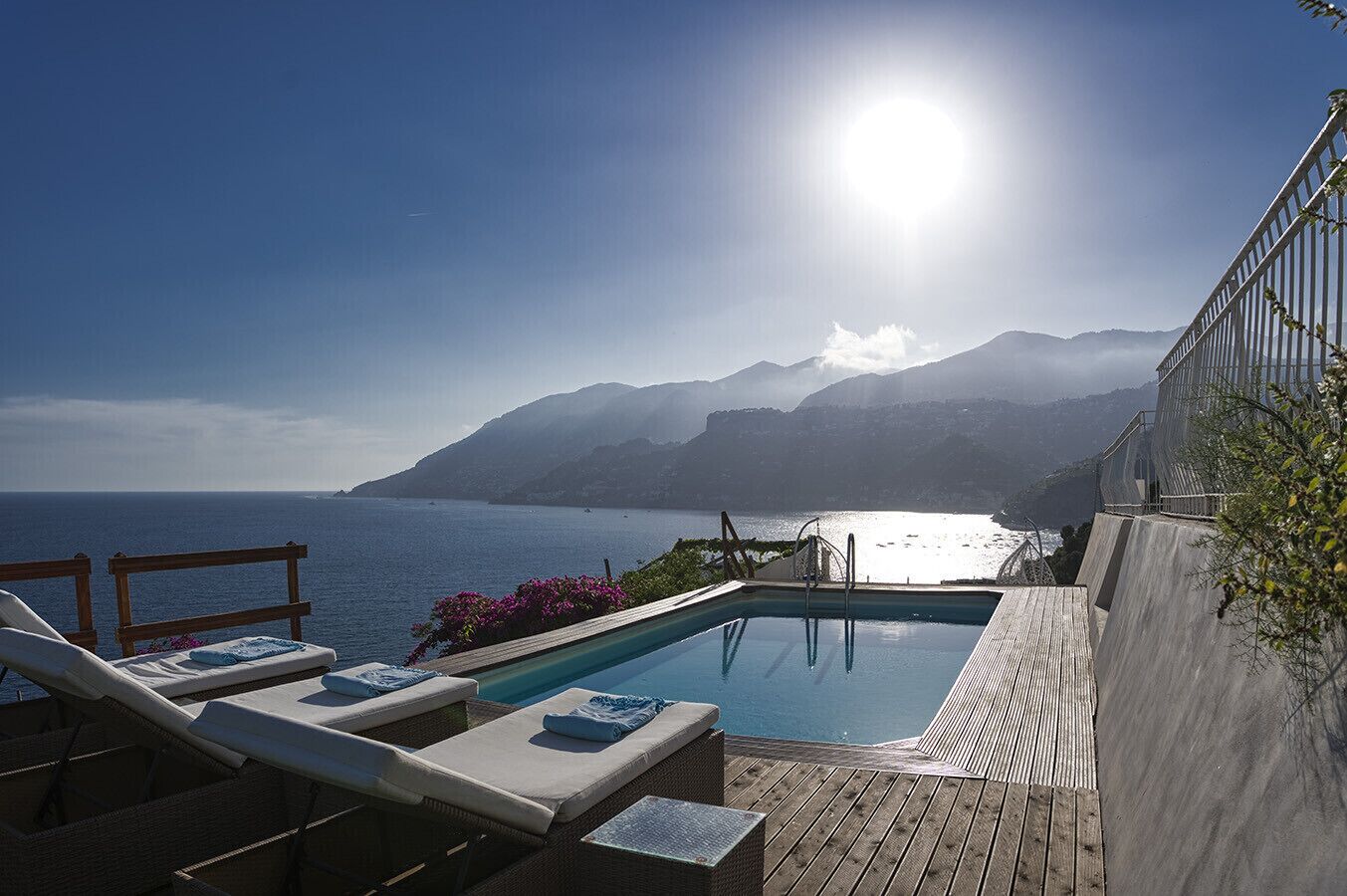 A pool with lounge chairs and a wooden deck overlooking a body of water and mountains.