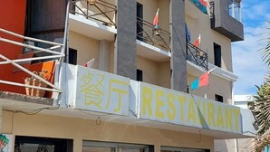 A multi-story building with balconies, a restaurant on the ground floor, and flags on the balconies. - Castello Motel (Antananarivo)