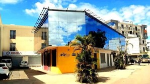 A modern building with a glass facade, a small orange structure with 'MVola' signage, and a 'XINDA' sign on a nearby building. - Castello Motel (Antananarivo)