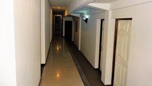 A long, narrow hallway with white walls and a tiled floor. There are doors on both sides, and a light fixture is visible on the right wall. - Castello Motel (Antananarivo)