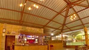 An indoor dining area with a high, curved metal roof and wooden tables and chairs.