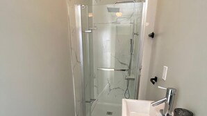 Ein schmales Badezimmer mit Duschkabine aus Glas, einem weißen Waschbecken und einem kleinen Schrank.