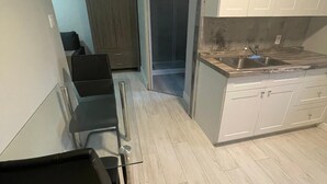 Une cuisine de taille réduite avec des meubles blancs, un évier en acier inoxydable et un plancher en bois.