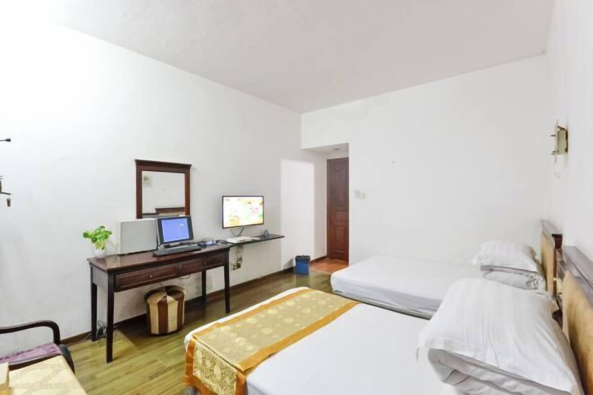 Habitación de hotel con dos camas individuales, un escritorio con computadora, una silla y una pequeña mesa con una planta.