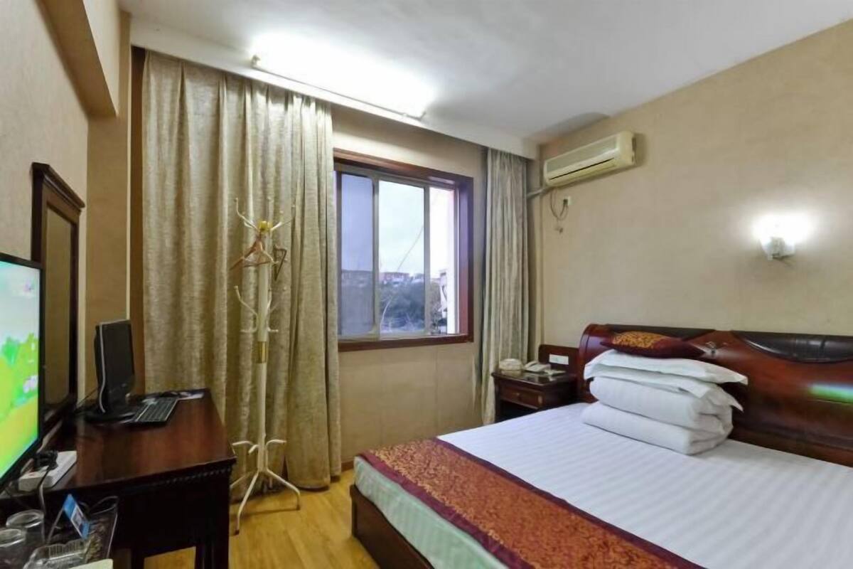Habitación de hotel con cama, escritorio con computadora, televisión y ventana con cortinas.