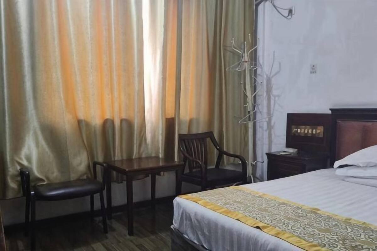 Una habitación de hotel con cama, escritorio, dos sillas, mesita de noche y ventana con cortinas.