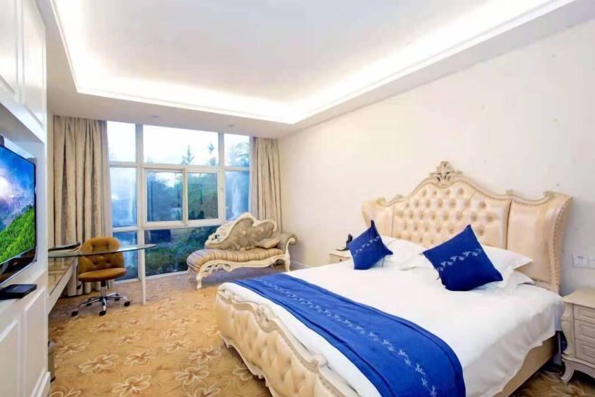 Un dormitorio con una cama grande, televisión y una ventana con cortinas.