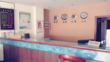 A reception desk with a wooden counter and a glass partition, a red chair, and wall clocks.