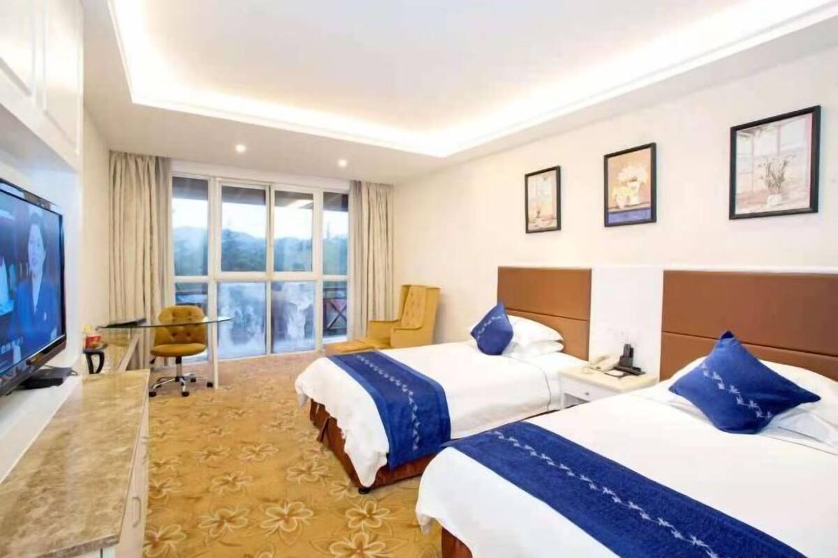 Habitación de hotel con dos camas, televisión, escritorio y ventana con vistas.