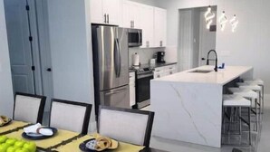 Une cuisine moderne dotée d’appareils électroménagers en acier inoxydable, d’un îlot en marbre et d’un coin repas avec une table dressée pour deux personnes.
