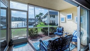 A covered patio with a view of a marina and buildings, featuring two blue-striped chairs and a small table. - Cozy 2 Bed 2 Bath Waterfront Condo SE Cape Coral only 20 min to Ft Myers Beach (Cape Coral)