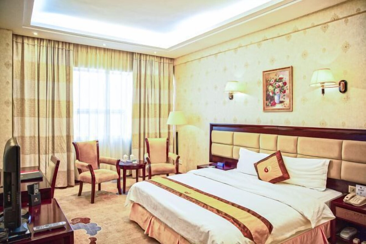 A hotel room with a large bed, two armchairs, a desk with a television, and a window with curtains.