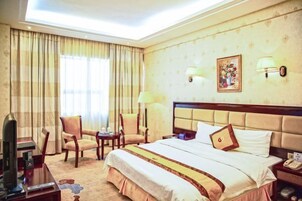 Habitación de hotel con una cama grande, dos sillones, un escritorio con televisor y una ventana con cortinas.