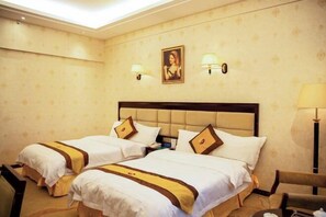 A hotel room with two beds, a headboard, wall-mounted lamps, a framed picture, and a chair. - Hexie Hotel (Zhenxiong)