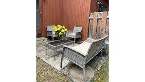 Un patio con mobiliario de mimbre, una mesita y un florero con flores amarillas.