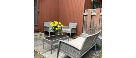 A patio area with wicker furniture, a small table, and a vase of yellow flowers.