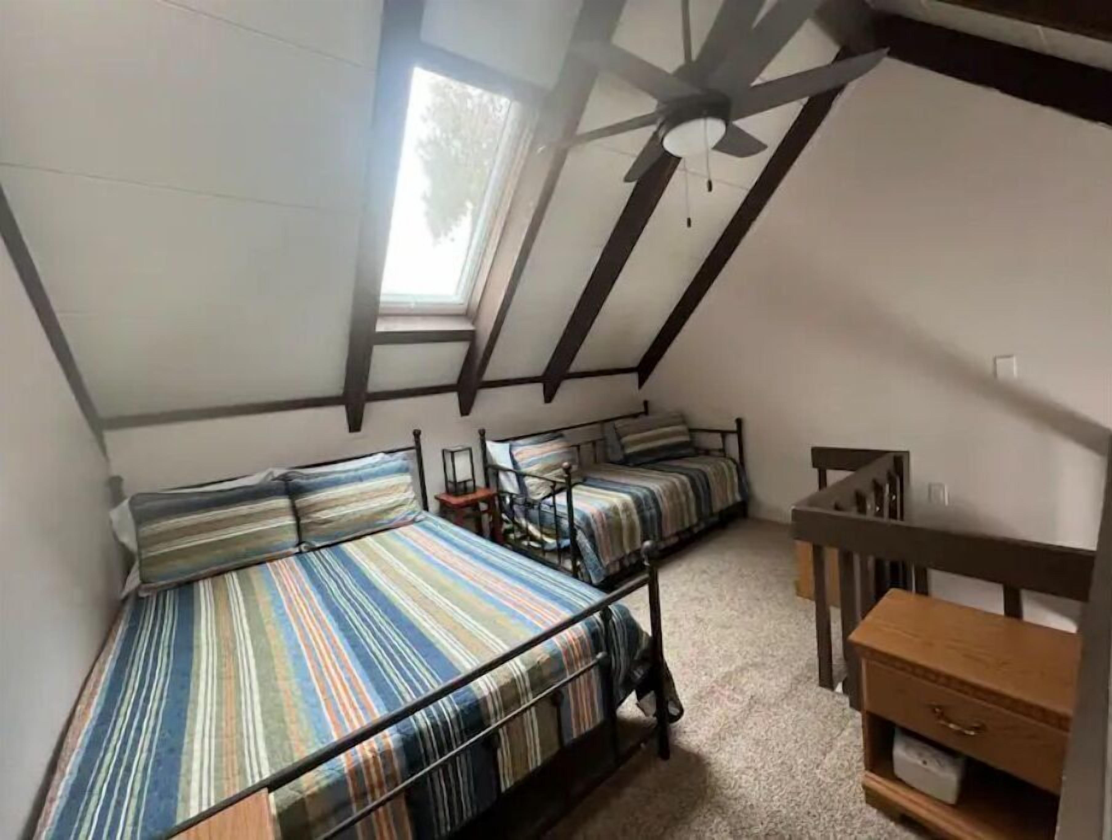 Un dormitorio con dos camas, un aparador de madera, un ventilador de techo y un tragaluz.