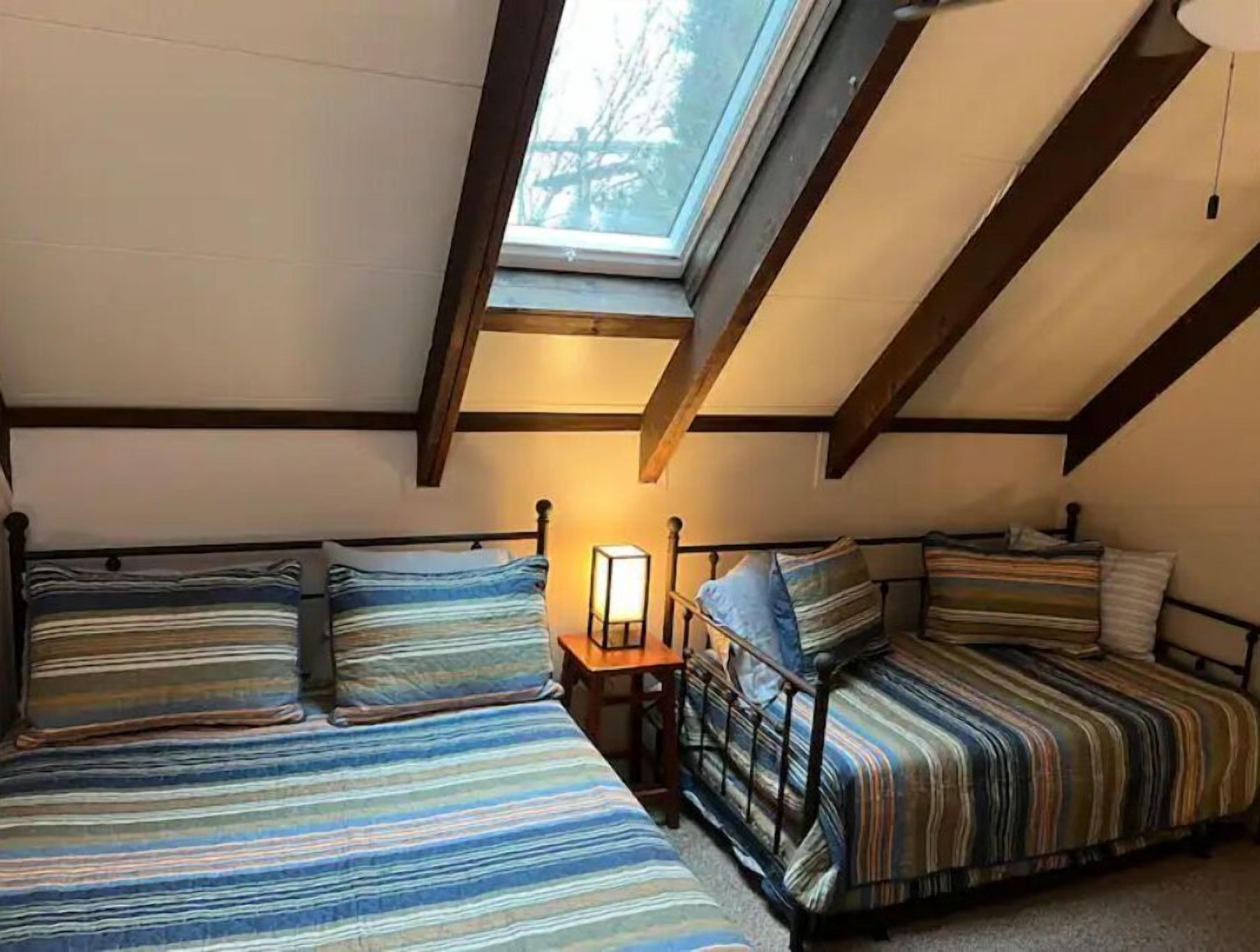 Quarto de dormitório com duas camas, um claraboia e uma mesa de cabeceira com abajur.