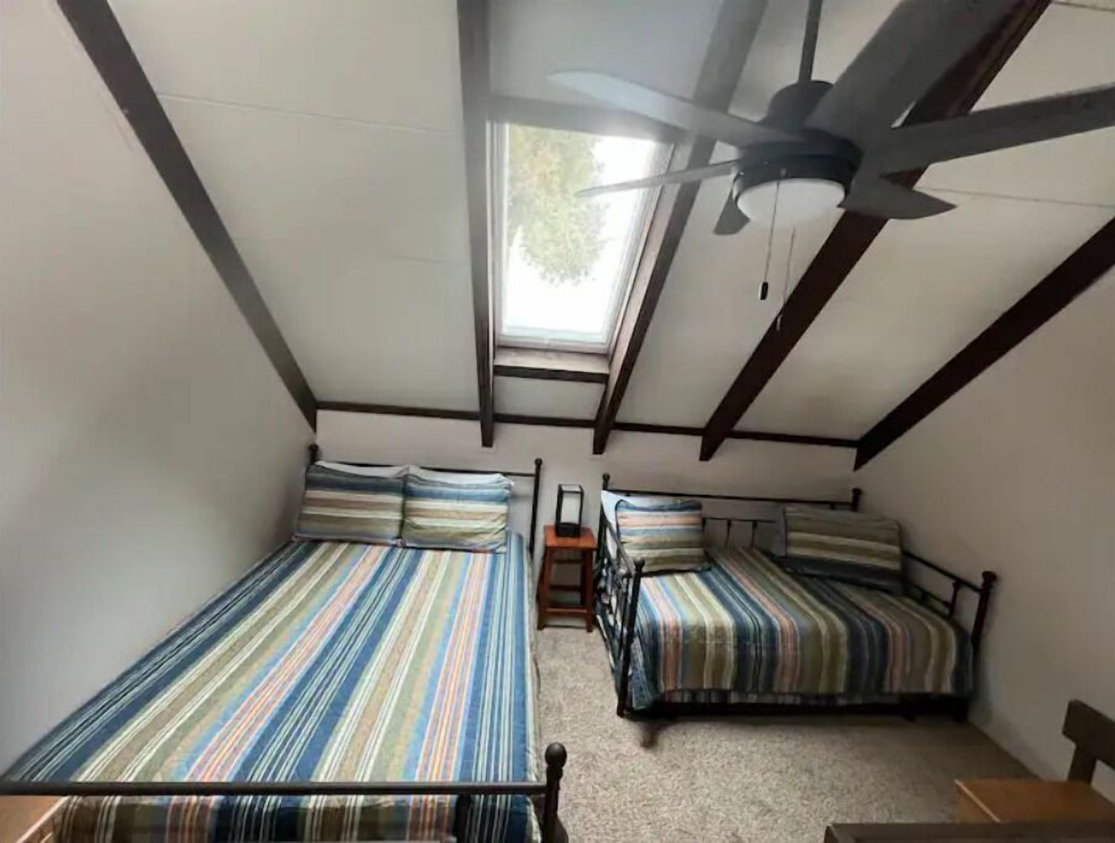 A small, attic-style room with two beds, a ceiling fan, and a skylight.