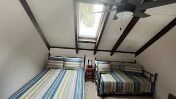 A small, attic-style room with two beds, a ceiling fan, and a skylight.