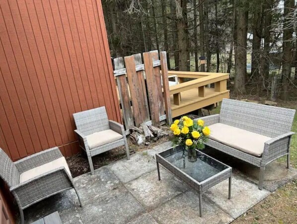 An outdoor seating area with wicker furniture and a glass table, surrounded by a wooden deck and a red wall.