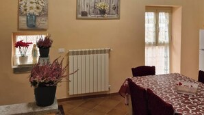 Un comedor con una mesa dispuesta para cuatro personas, un radiador y dos ventanas con cortinas.