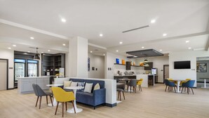 Una cocina moderna con una isla central, una zona de comedor con sillas amarillas y un espacio de sala con un sofá azul.