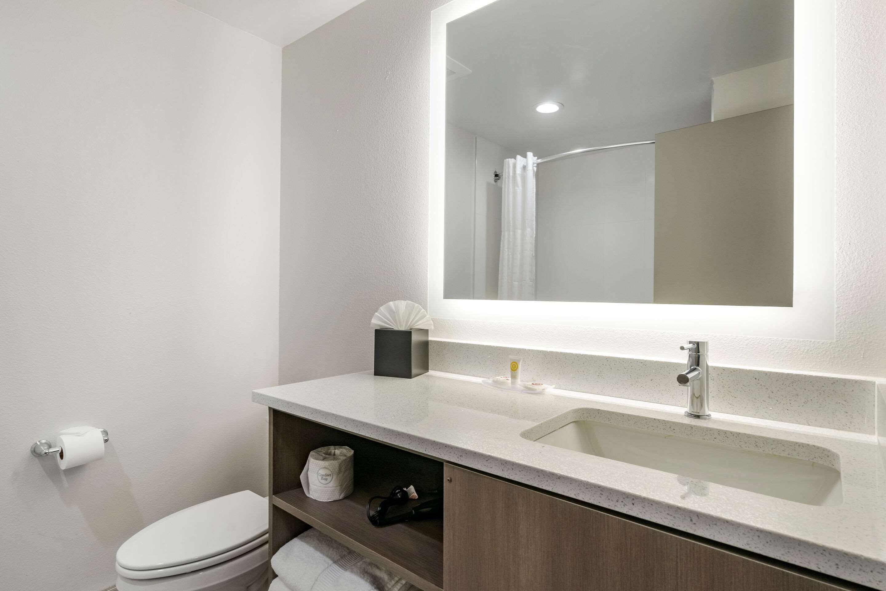 A modern bathroom with a white toilet, a sink with a mirror above it, and a shower curtain.