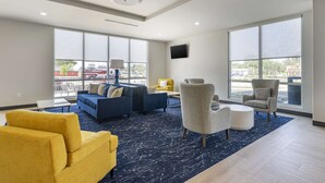 Un salón amplio con ventanas grandes, una alfombra azul y muebles modernos, incluyendo un conjunto de sofás y sillones.