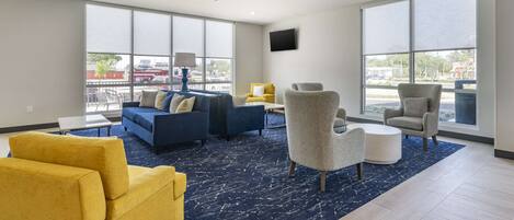 A spacious living room with large windows, a blue carpet, and modern furniture including a sofa set and armchairs.
