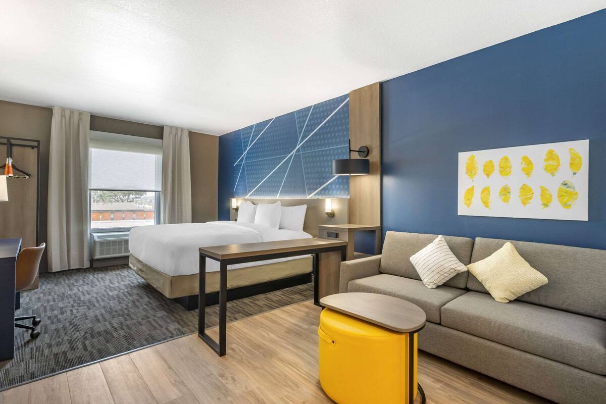 A hotel room with a bed, a sofa, a desk, and a window.
