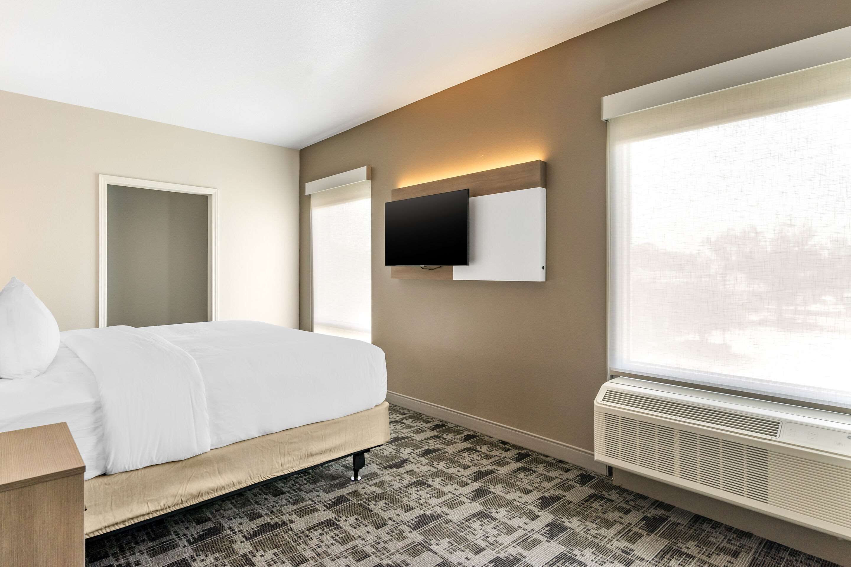 Ein Hotelzimmer mit Bett, Flachbildfernseher an der Wand, Fenster mit Aussicht und integrierter Klimaanlage.