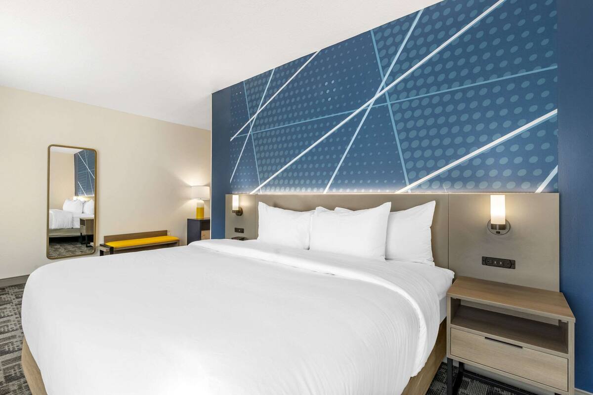 A hotel room with a large bed, a bench, a mirror, and a wall with geometric patterns.