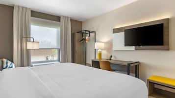 A hotel room with a large bed, a desk with a chair, a television mounted on the wall, and a window with curtains.