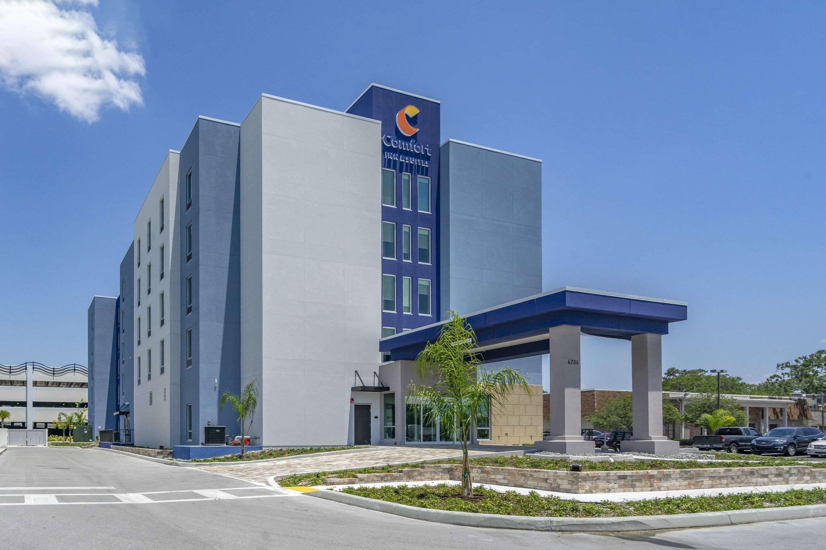 A modern hotel with a prominent blue and white facade, a covered entrance, and a parking area with cars.
